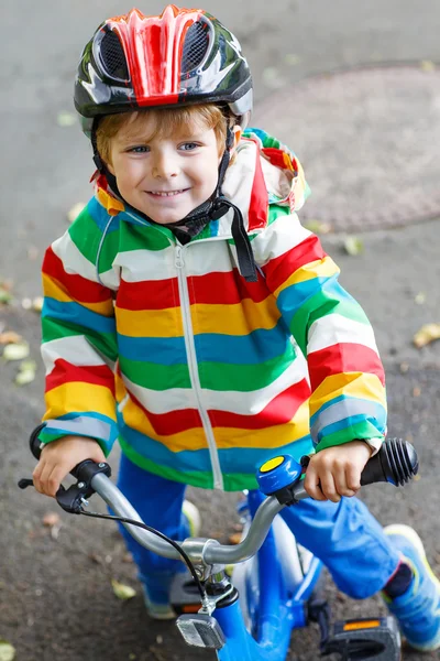 Adorable kid boy in red helmet and colorful raincoat riding his — Stock Photo, Image