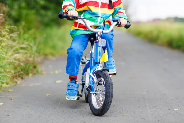 Criança em capa de chuva colorida montando sua primeira bicicleta — Fotografia de Stock