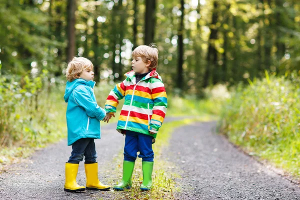 Zwei kleine Geschwister in bunten Regenmänteln und Stiefeln gehen — Stockfoto