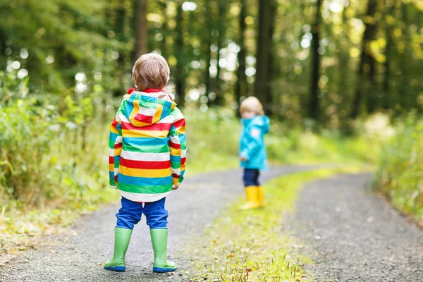 Deux petits frères et sœurs en imperméables colorés et bottes marchant — Photo