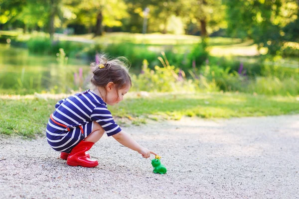 Красивая маленькая девочка в красных ботинках дождя играет с резиновой лягушкой — стоковое фото