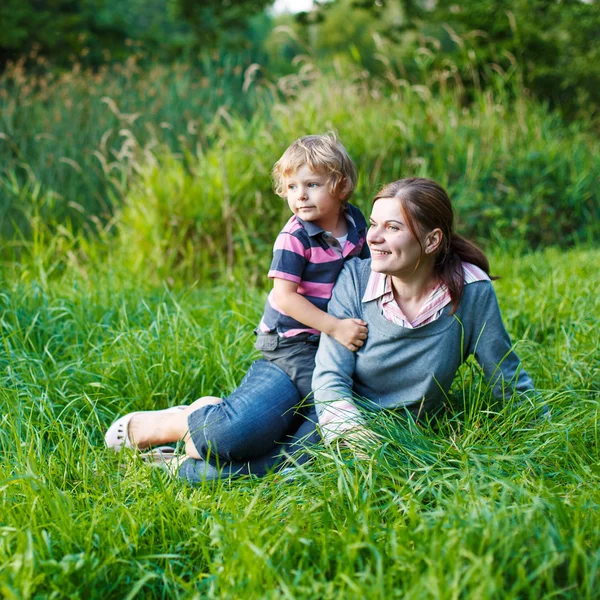 Little boy and his mother sitting on grass in summer forest — Stock Photo, Image