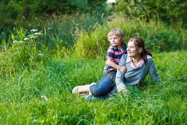Little boy and his mother sitting on grass in summer forest — Stock Photo, Image