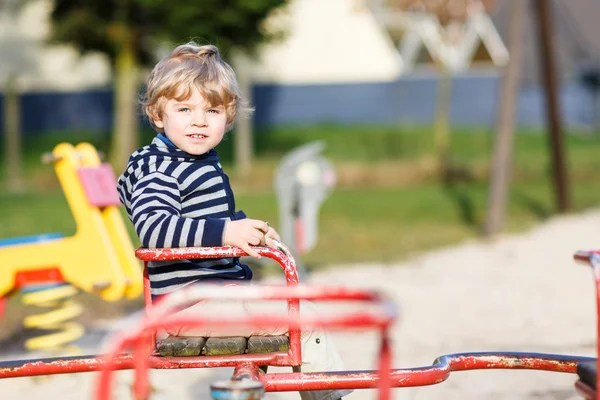 Piccolo bambino ragazzo avendo divertente su vecchio giostra su all'aperto playgro — Foto Stock