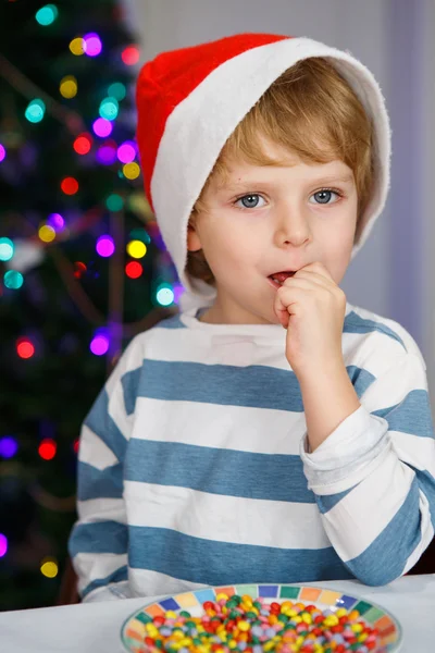 Petit garçon en chapeau de Père Noël avec arbre de Noël et lumières — Photo