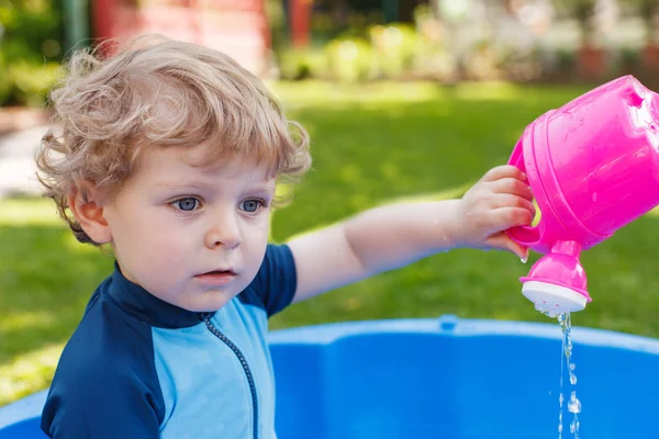 Schattige blonde peuter jongen spelen met water, buitenshuis. — Stockfoto