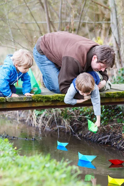 Two little brothers and their dad playing with paper boats by a — Stock Photo, Image