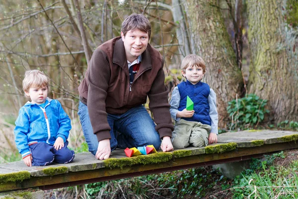 Two little brothers and their dad playing with paper boats by a — Stock Photo, Image