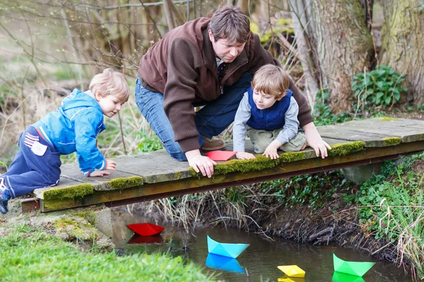 Dos hermanos pequeños y su padre jugando con barcos de papel por un — Foto de Stock