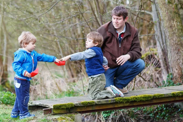 Two little brothers and their dad playing with paper boats by a — Stock Photo, Image