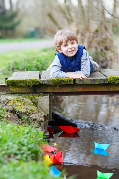 Adorable niño jugando con coloridos barcos de papel por un r —  Fotos de Stock