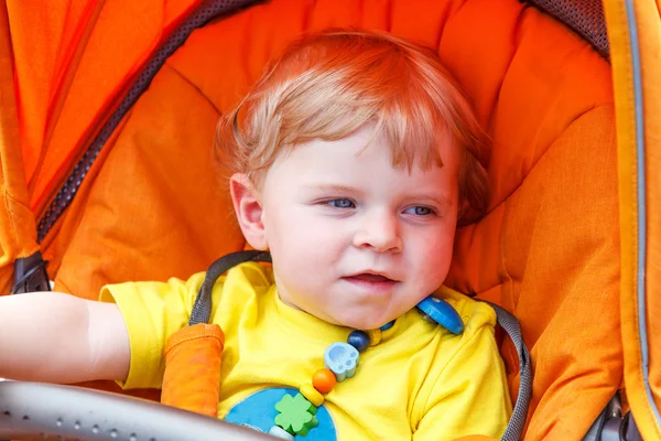 Lindo menino da criança sorrindo ao ar livre em carrinho de bebê laranja — Fotografia de Stock