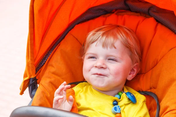 Grappige peuter jongen glimlachend buiten in oranje wandelwagen — Stockfoto