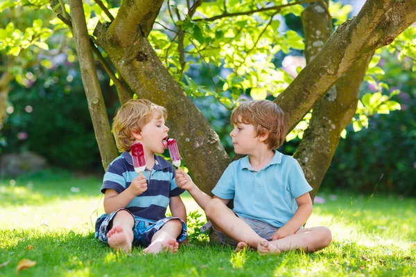 Zwei kleine Geschwister essen rotes Eis im heimischen Garten. — Stockfoto