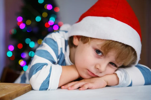 Little boy in santa hat with christmas tree and lights Stock Picture