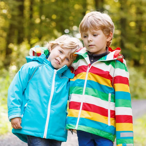Two little sibling boys in colorful raincoats and boots walking — Stock Photo, Image