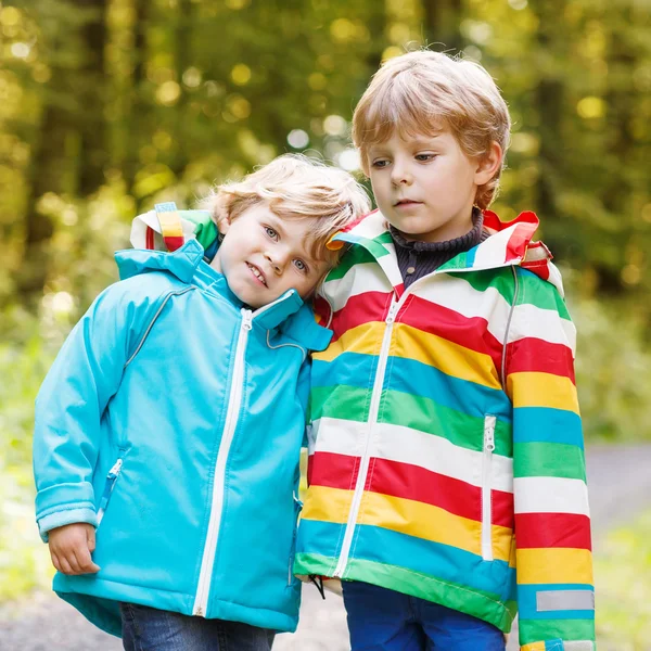 Dos niños hermanos pequeños en coloridos impermeables y botas caminando — Foto de Stock