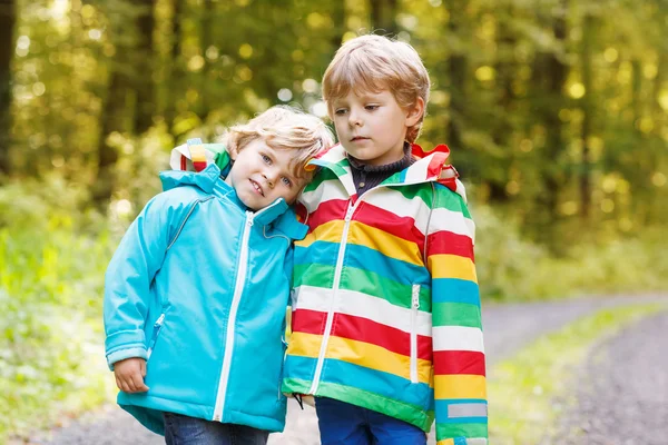 Two little sibling boys in colorful raincoats and boots walking — Stock Photo, Image