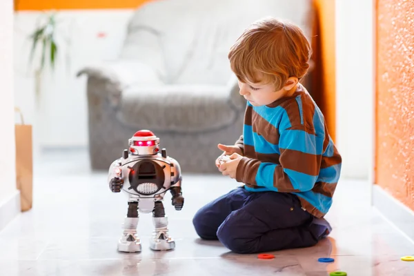 Pequeño chico rubio jugando con robot de juguete en casa, interior . — Foto de Stock