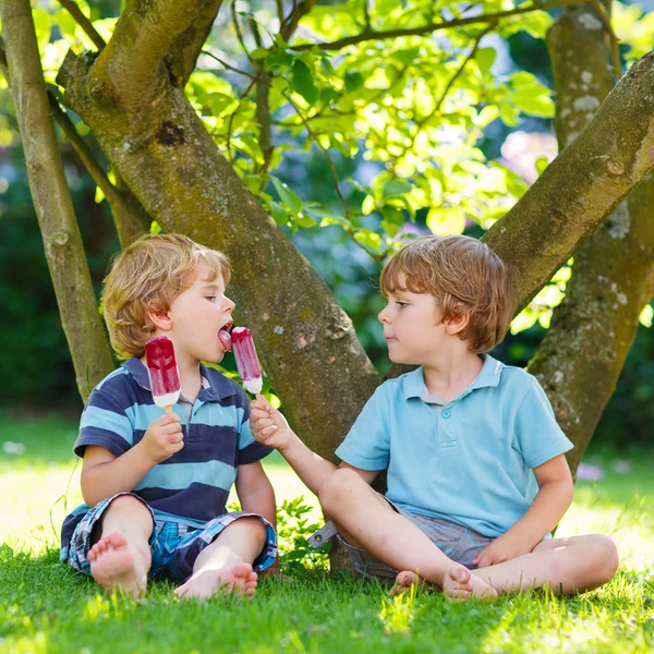 Zwei kleine Geschwister essen rotes Eis im heimischen Garten. — Stockfoto