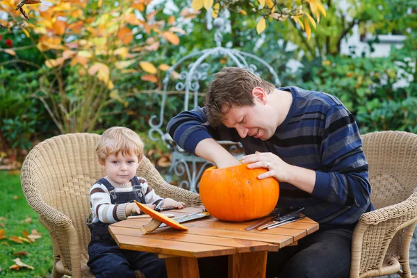 Jonge man en peuter jongen halloween pompoen maken — Stockfoto