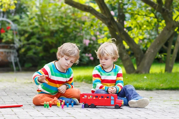 Dois meninos irmãos brincando com ônibus escolar vermelho — Fotografia de Stock