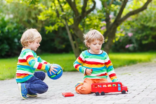 Двое братьев и сестер, мальчики играют с красным школьным автобусом — стоковое фото