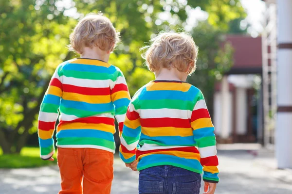 Two little sibling children in colorful clothing walking hand in — Stock Photo, Image