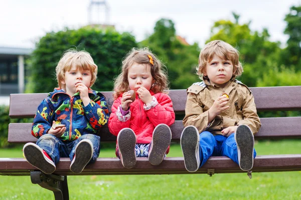 Два маленьких мальчика и одна девочка едят шоколад — стоковое фото