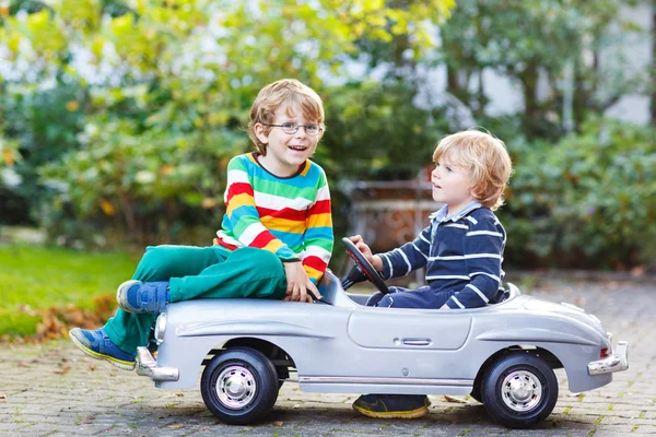 Zwei glückliche Kinder spielen mit großem alten Spielzeugauto im Sommergarten, ou — Stockfoto