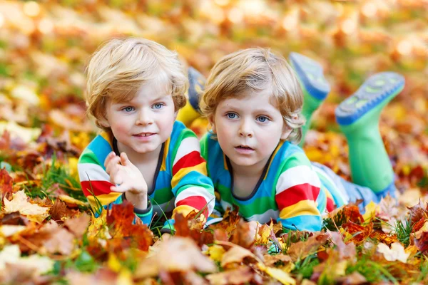 Two little kid boys laying in autumn leaves in colorful clothing — Stock Photo, Image