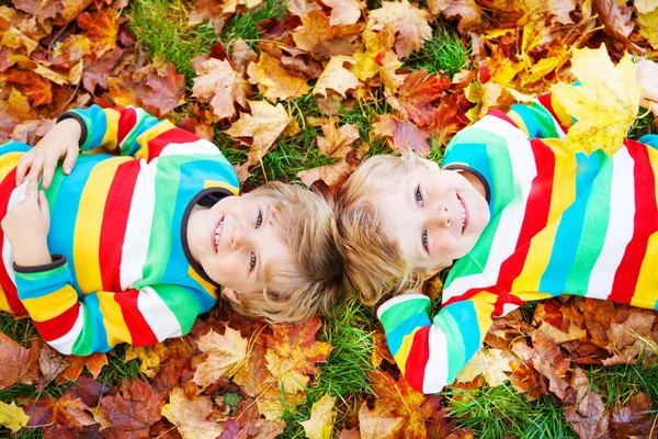 Twee kid weinig jongens leggen in herfst bladeren in kleurrijke kleding — Stockfoto