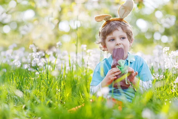Niño pequeño con orejas de conejo de Pascua y comer chocolate en s —  Fotos de Stock
