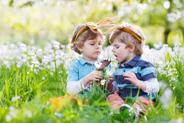 Twee kleine jongens dragen Easter bunny oren en het eten van chocolade — Stockfoto
