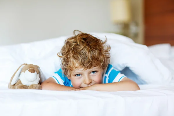 Adorable kid boy after sleeping in his white bed with toy — Stock Photo, Image