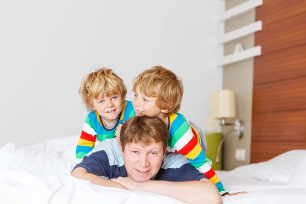 Dos niños hermanos y papá divirtiéndose en la cama después de dormir —  Fotos de Stock