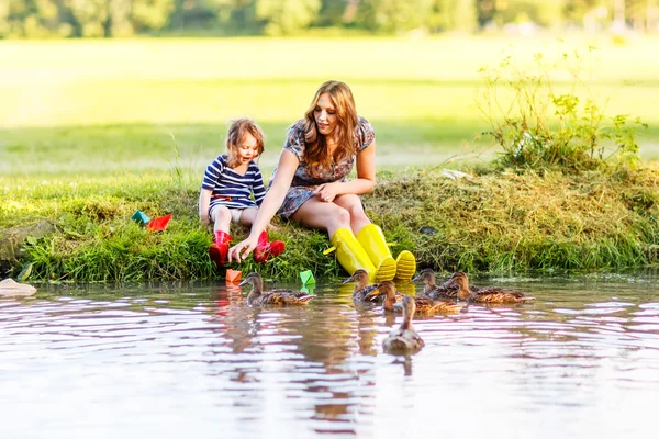 Bedårande liten flicka och hennes mamma leker med papper båtar i ett r — Stockfoto