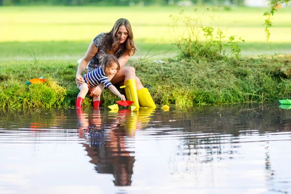 Adorabile bambina e sua madre giocare con barche di carta in un r — Foto Stock