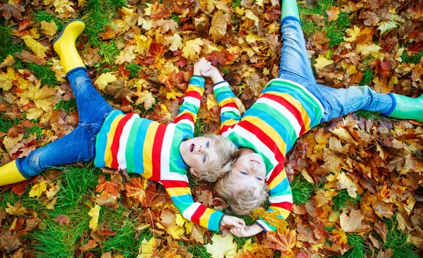 Two little kid boys laying in autumn leaves in colorful clothing — Stock Photo, Image