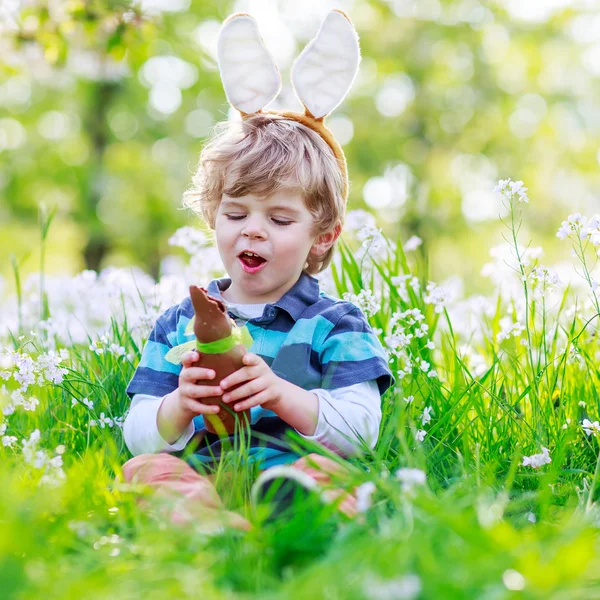 Bonito menino feliz vestindo orelhas de coelho da Páscoa e comer choco — Fotografia de Stock