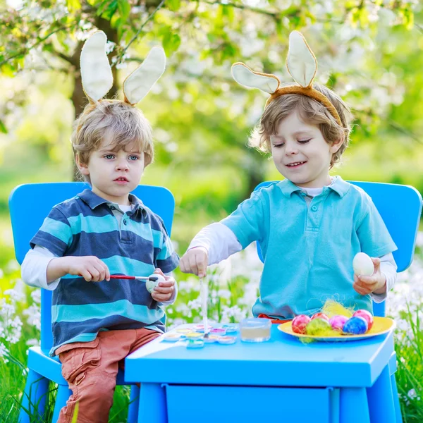 Two little twin boys in Easter bunny ears coloring eggs — Stock Photo, Image