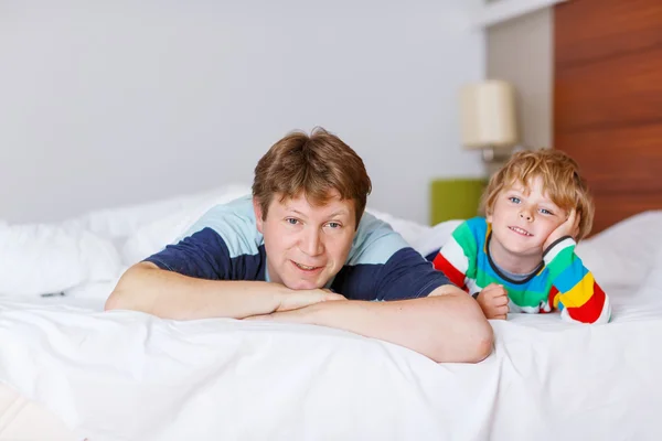 Father and his little kid son relaxing and resting in white bed Stock Photo