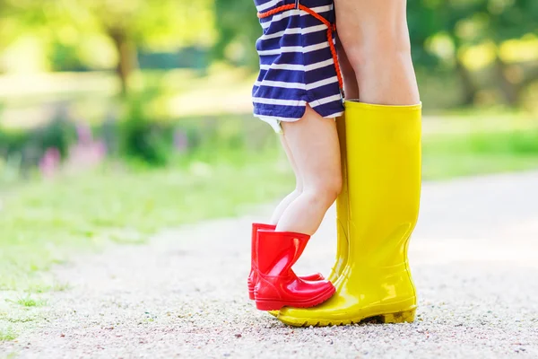 Las piernas de la mujer joven y su hija pequeña hija en botas de lluvia —  Fotos de Stock