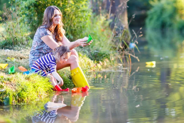 Entzückendes kleines Mädchen und ihre Mutter spielen mit Papierbooten in einem r — Stockfoto