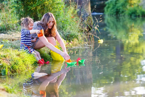 Adorable little girl and her mom playing with paper boats in a r — Stock Photo, Image