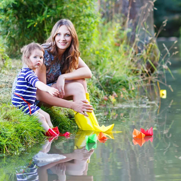 Entzückendes kleines Mädchen und ihre Mutter spielen mit Papierbooten in einem r — Stockfoto