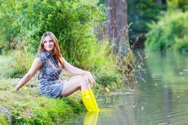 Młoda piękna kobieta siedzi w żółty deszcz guma łodzie przez r — Zdjęcie stockowe