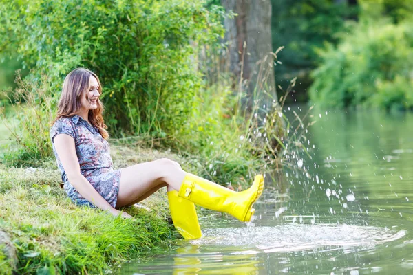 Jonge mooie vrouw zitten in geel regen rubberboten door een r — Stockfoto
