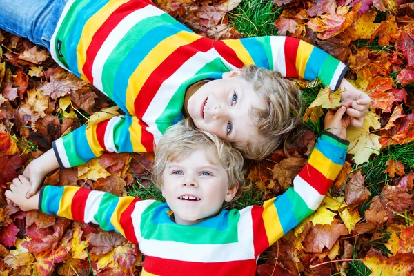 Zwei kleine Jungen liegen in bunten Kleidern im Herbstlaub — Stockfoto