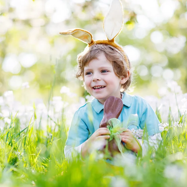 Little toddler wearing Easter bunny ears and eating chocolate at Stock